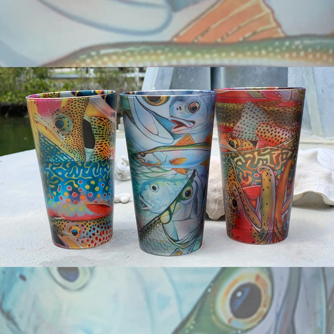 Three colorful fish-patterned tumblers on a white surface with a blurred outdoor background.
